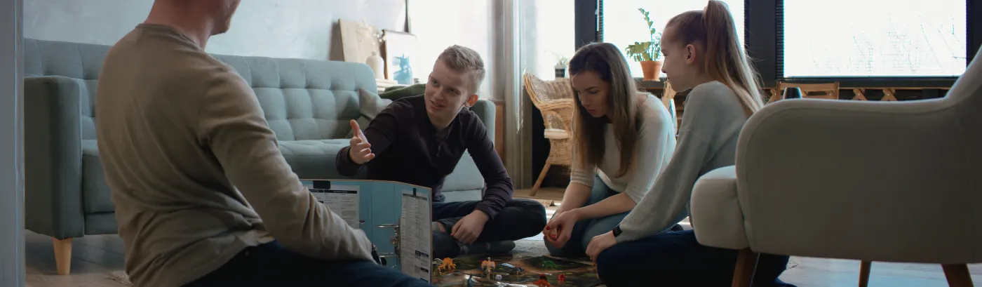 Teens and an adult game master playing a tabletop game together on the living room floor